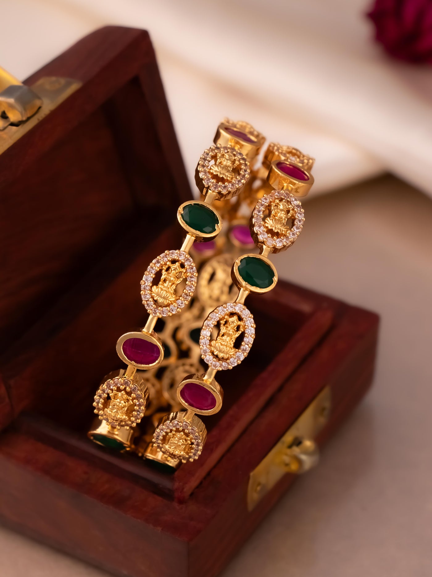 Oval-shaped Laxmi bangles with CZ and ruby-green Kemp stones in gold. A perfect blend of tradition and elegance.

