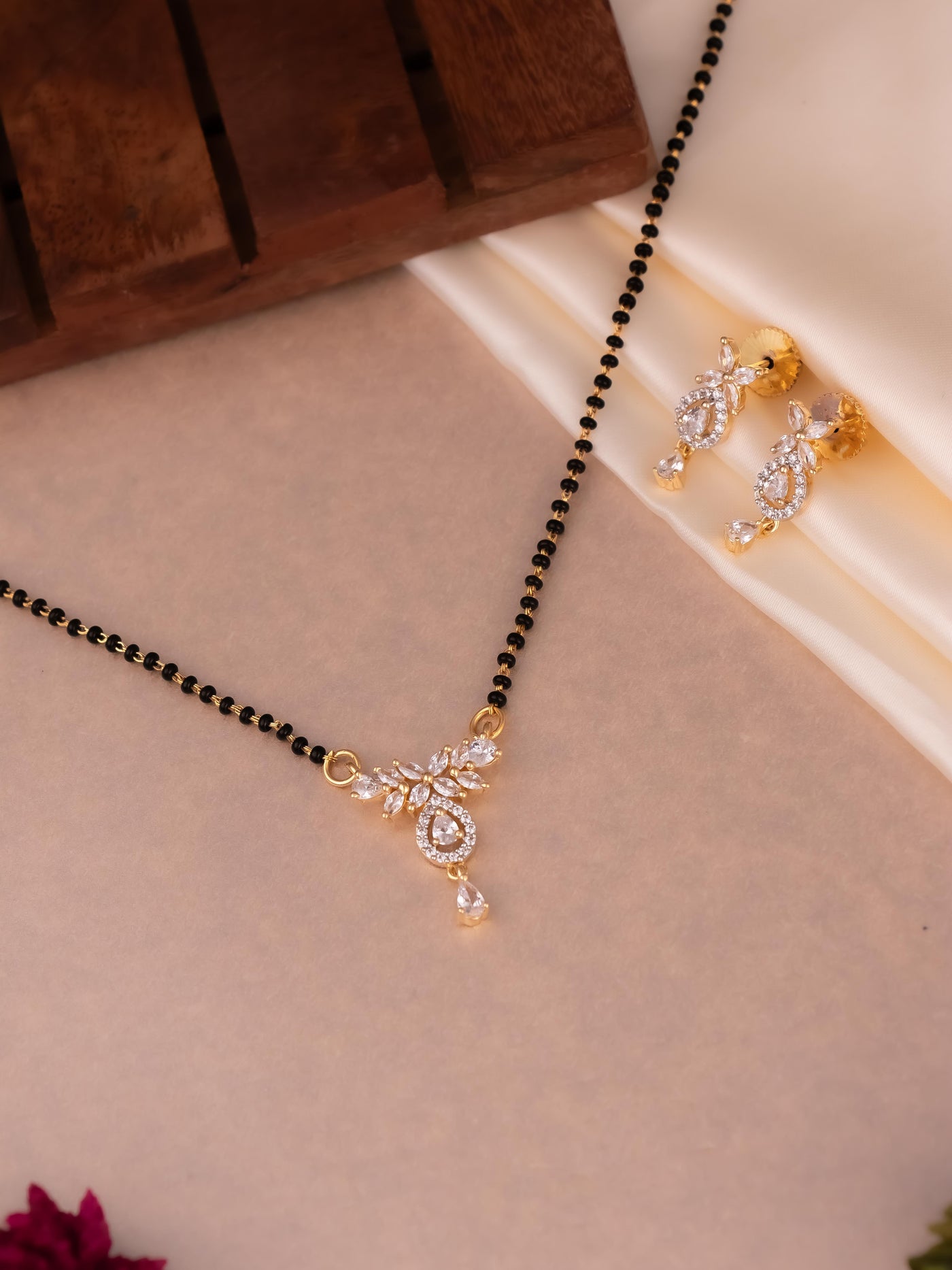 Unique flower pattern drop Mangalsutra in gold polish with diamond stones, includes a matching pair of earrings.
